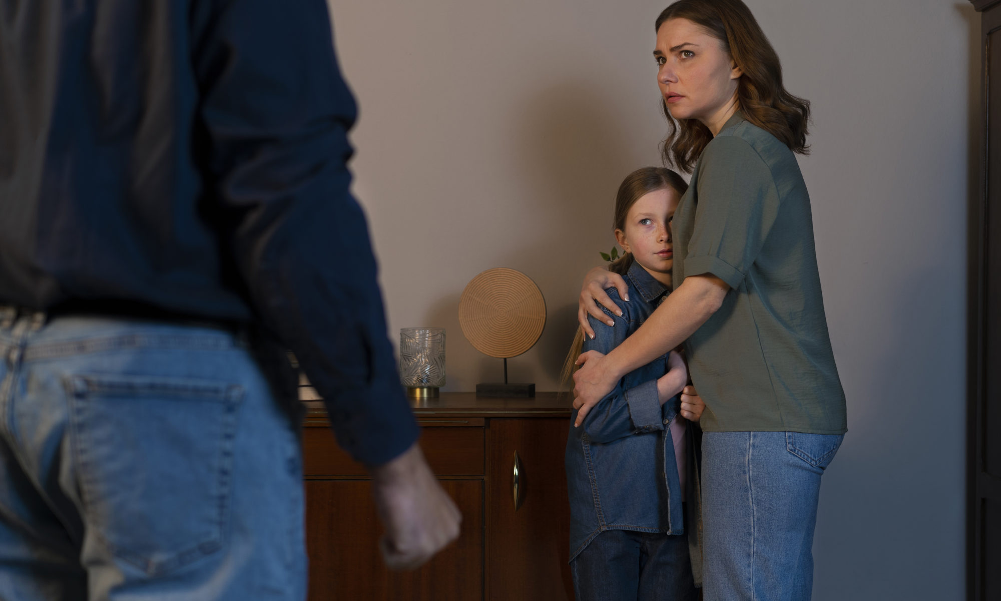 A mother protectively hugging her daughter during a tense moment with the co-parent, illustrating the emotional impact of high-conflict co-parenting and the importance of child safety in separated families.