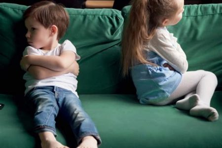 Deux jeunes enfants assis dos à dos sur un canapé, boudant l’un et l’autre.