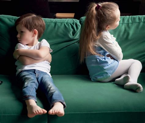 Deux jeunes enfants assis dos à dos sur un canapé, boudant l’un et l’autre.