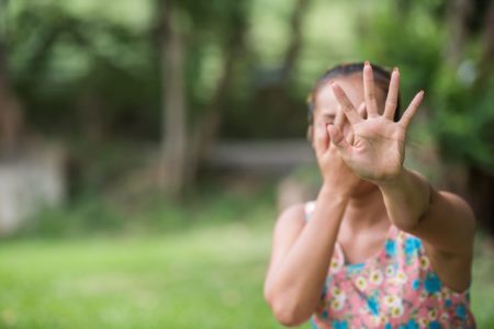 A woman in a floral dress holds up her hand toward the camera in a clear “stop” gesture while covering part of her face, expressing fear or distress. The blurred natural background contrasts with her emotional state—highlighting the urgency of protecting oneself from an ex-partner’s harassment and establishing safe, respectful co-parenting boundaries.