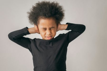 Highly sensitive child covering ears and closing eyes in distress, symbolizing the emotional challenges kids face in co-parenting situations and the need for supportive parenting strategies.