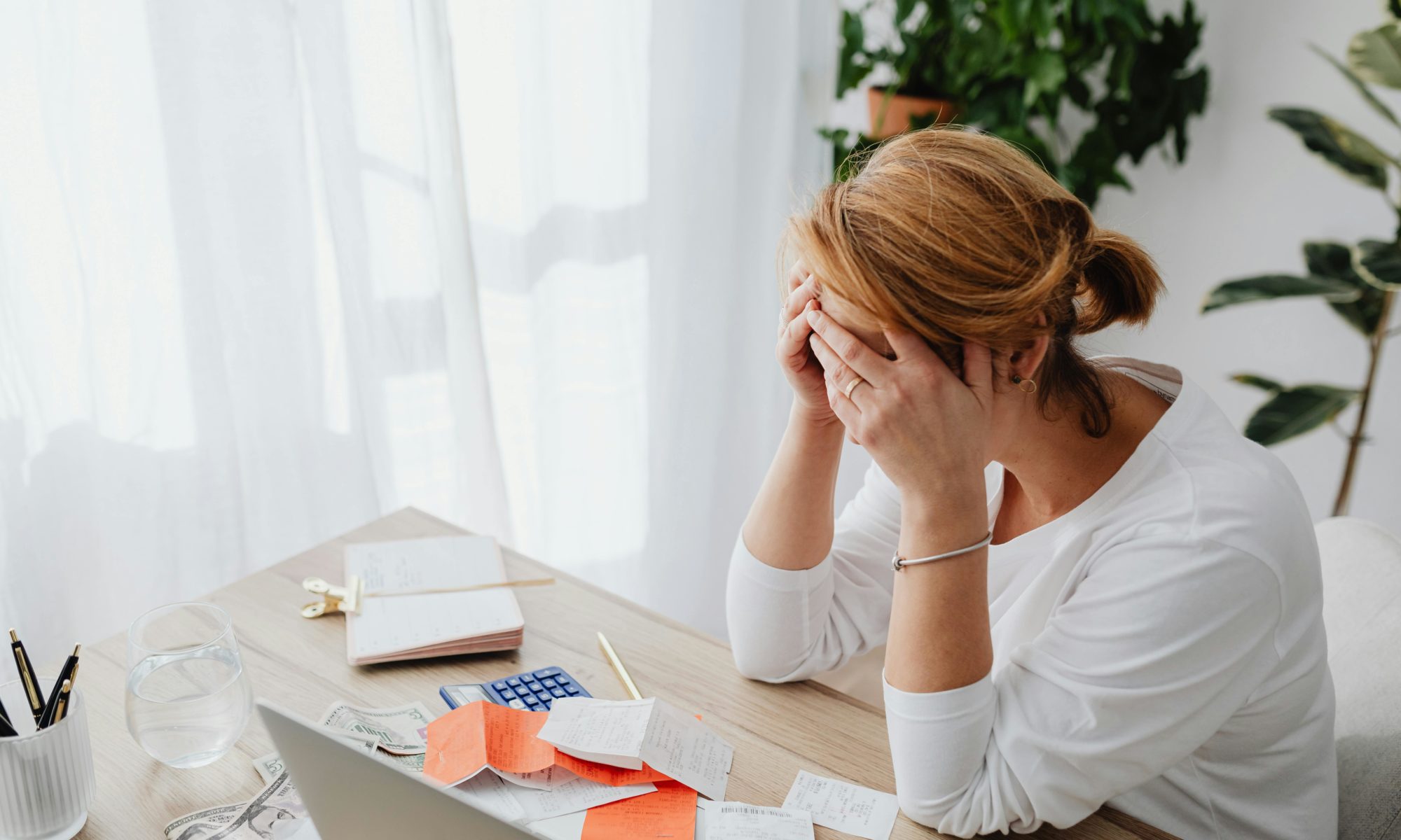 Stressed woman sitting at a desk with bills and a calculator, representing the mental load and financial mistakes to avoid in a parenting plan with a narcissistic co-parent.