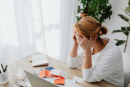 Stressed woman sitting at a desk with bills and a calculator, representing the mental load and financial mistakes to avoid in a parenting plan with a narcissistic co-parent.