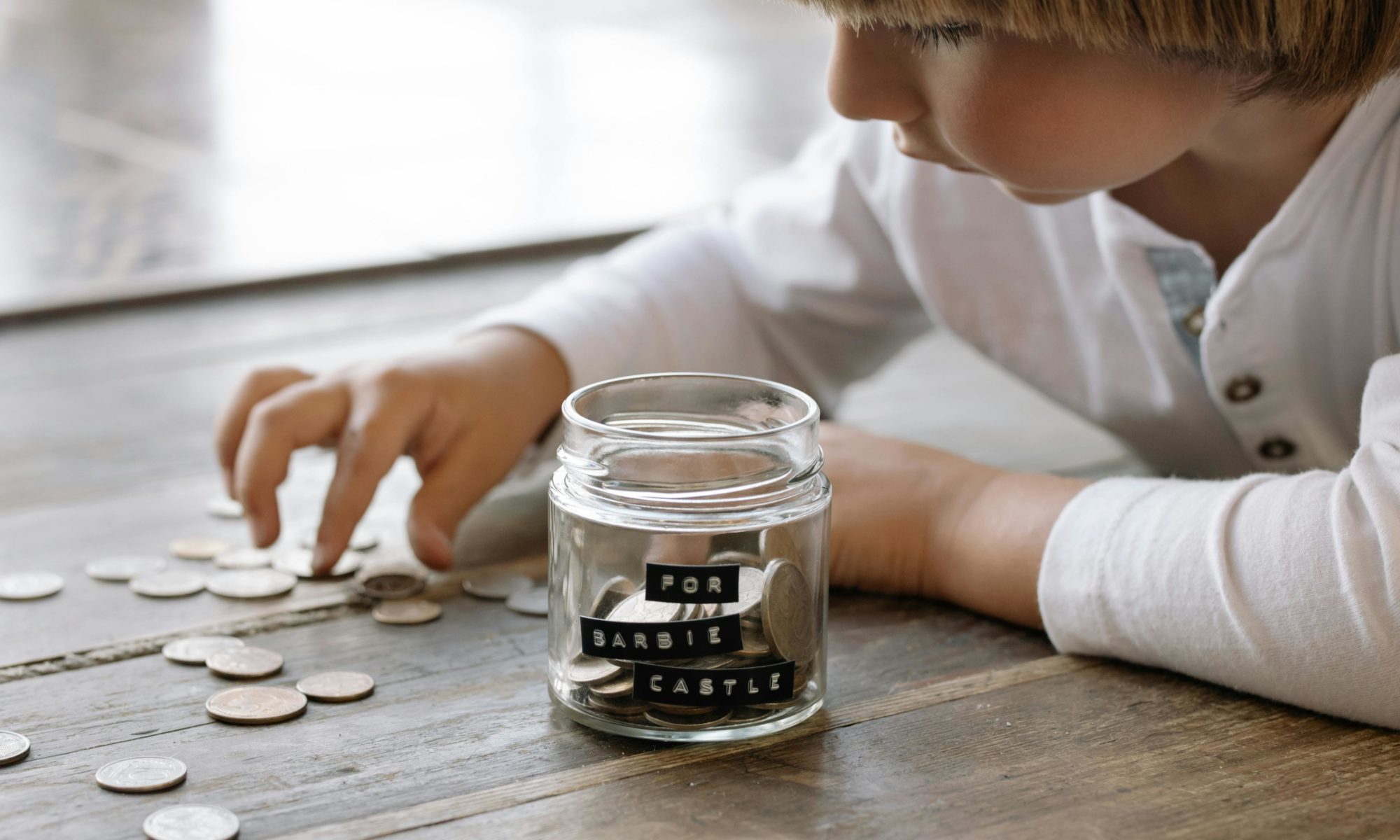 Ein Kind zählt Münzen neben einem Glas mit der Aufschrift „For Barbie Castle“ – Symbol für gemeinsames Sparen und faire finanzielle Planung in der Coparenting-Familie.