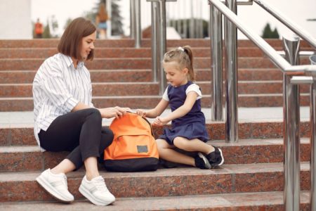 Transition entre deux foyers après une séparation : parent et enfant avec sac d'école devant l'école
